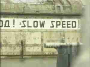 Painted sign reading SLOW SPEED on a harbor wall at a Northern Fleet submarine base, archival frame from Kursk submarine coverage.