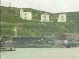 Apartment blocks on a hillside above a submarine base harbor, archival frame from Kursk submarine coverage.