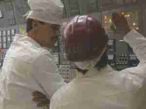 Workers in white overalls and a red hard hat at a control panel, archival frame from Chernobyl nuclear accident coverage.