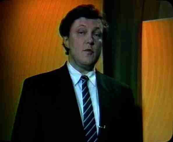 Archive television frame from the 1995 election campaign in Russia, a man in a dark suit and striped tie against an orange studio background
